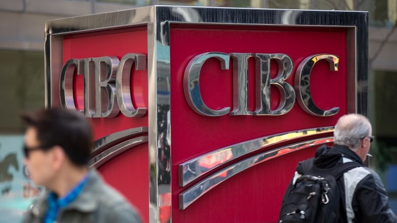 Pedestrians walk in front of a CIBC logo