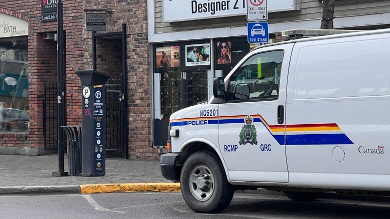 A white RCMP van is parked outside a business near a parkade.