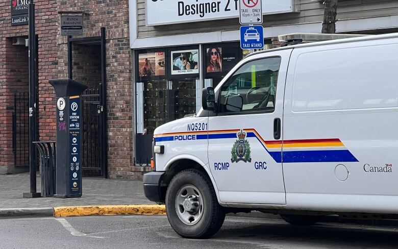 A white RCMP van is parked outside a business near a parkade.