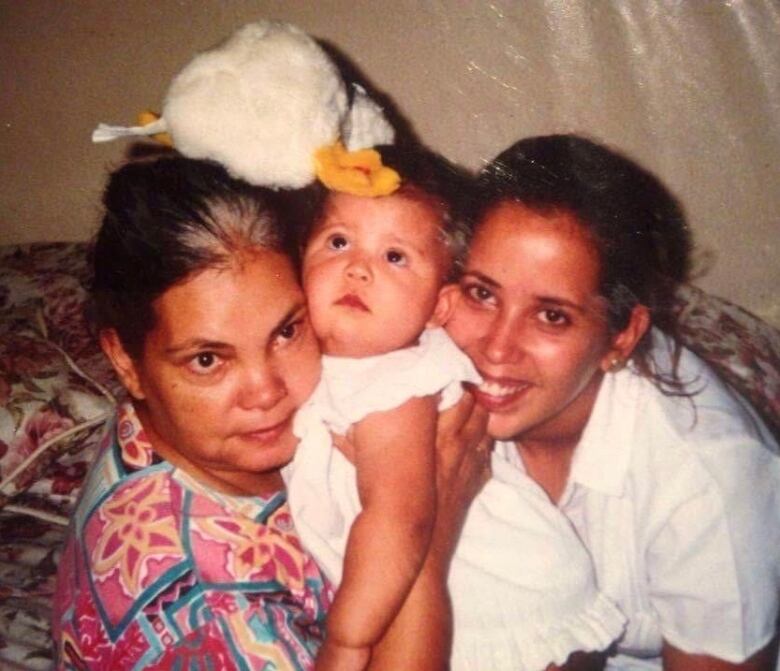 A baby being hugged and held by two women, one older.