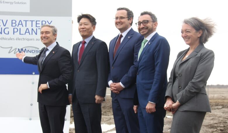 A group of people i suits stand in the wind in front of a sign. 