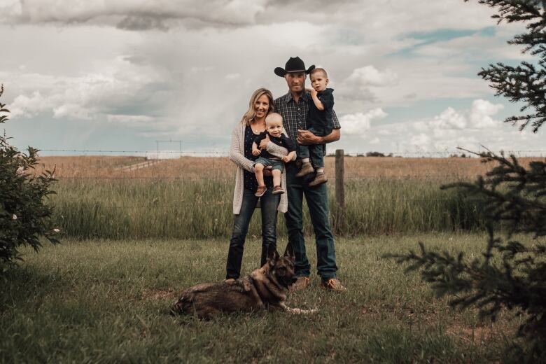 A man and woman holding two small children stand before a field. 