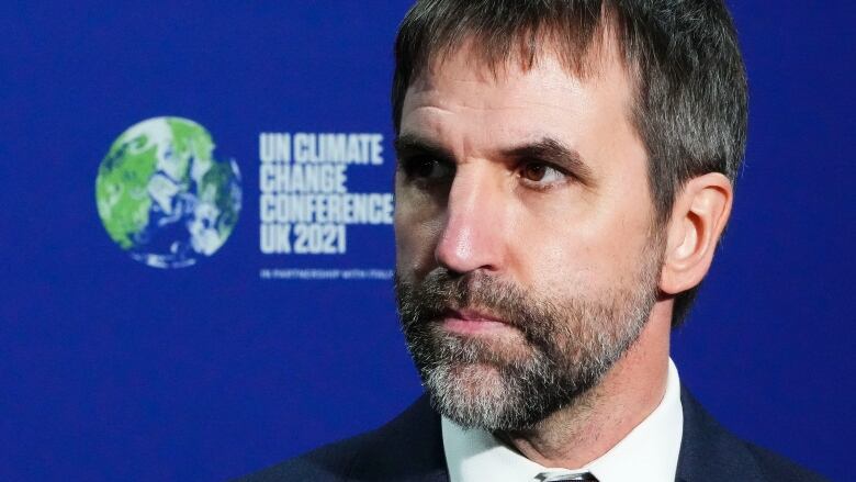 A bearded man stands in front of a sign that says UN Climate Change Conference UK 2021