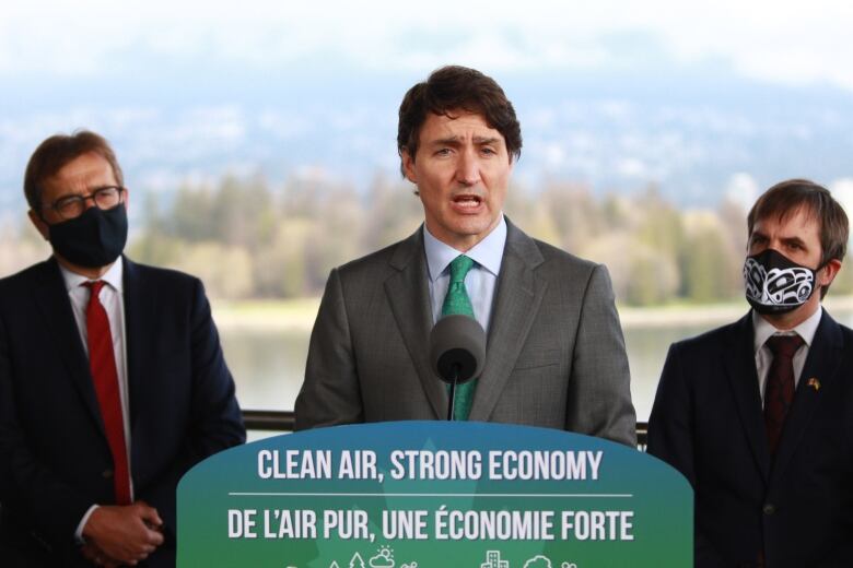 Three men, two of them masked, stand behind a podium.