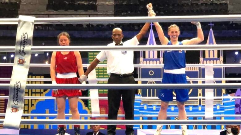 Three people stand in a boxing ring,  man with a woman on either side. He is holding up the arm of the woman on the right.