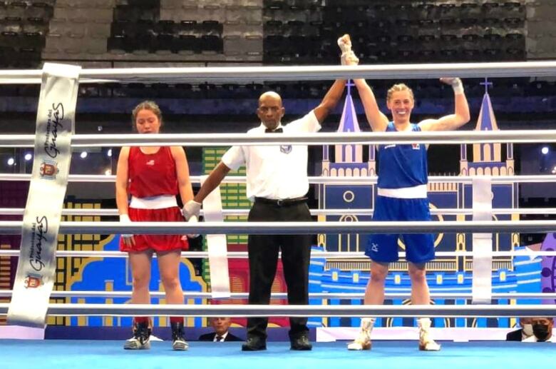 Three people stand in a boxing ring,  man with a woman on either side. He is holding up the arm of the woman on the right.