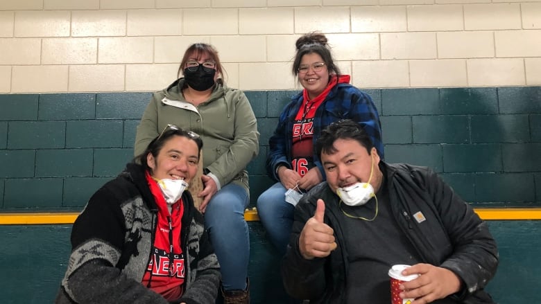 A group of people sit in hockey stands smiling as they pose for a photo. The father has his thumbs up. 