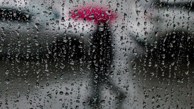 A man is seen with a red umbrella in silhouette as rain drops cover the camera lens.