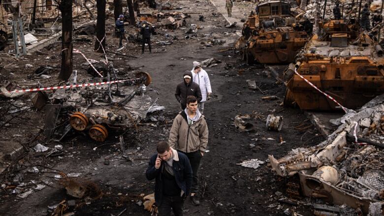 People walk along a heavily damaged street strewn with rubble, debris and destroyed vehicles.