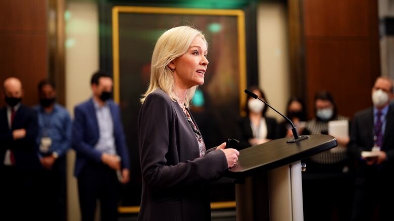 A blonde haired woman speaks at a podium.