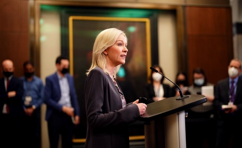 A blonde haired woman speaks at a podium.