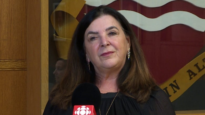 Vianne Timmons stands next to the Memorial University ceremonial coat of arms. 