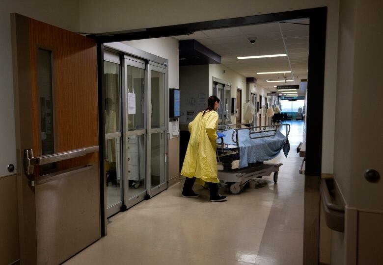 A health-care worker wearing a yellow medical gown transports a deceased COVID-19 patient on a stretcher, covered with a blue sheet, to the hospital morgue.