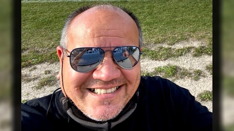 A man in aviator sunglasses smiles for the camera with a lawn in the background.