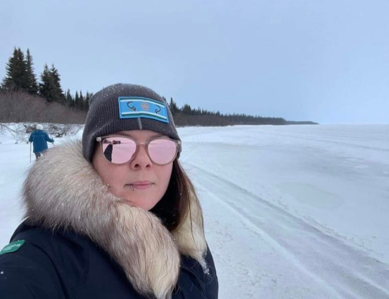 A woman wearing a coat with a fur hood stands on a frozen lake.