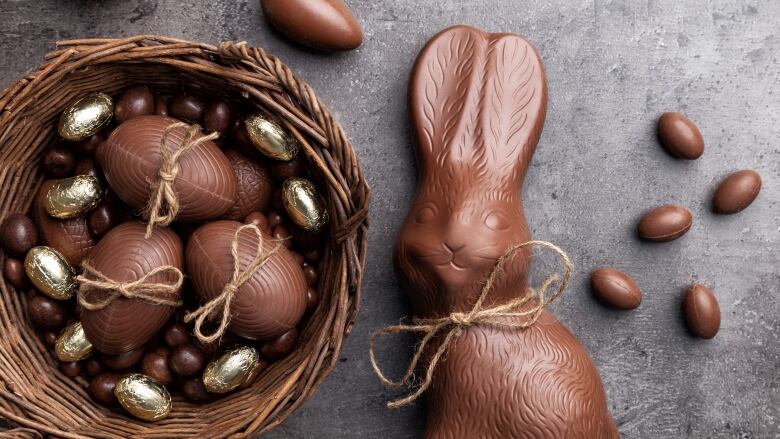 A chocolate bunny beside a pile of chocolate eggs.