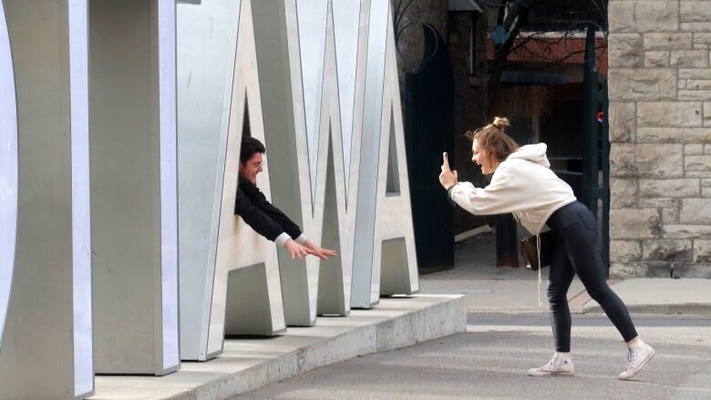 One person takes a photo of someone sticking through a gap in the 'A' of an 'OTTAWA' sign.