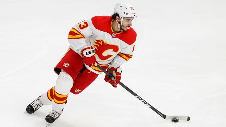 A man in a calgary flames hockey uniform skates while holding a hockey stick. he is a hockey player.