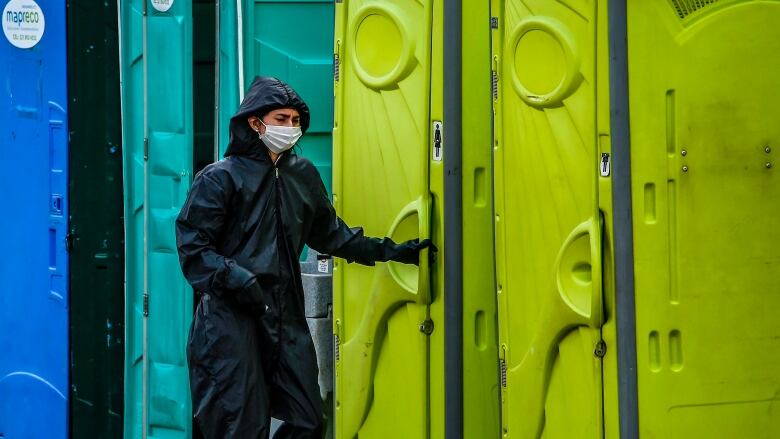 A woman wearing a mask stands outside public toilets.