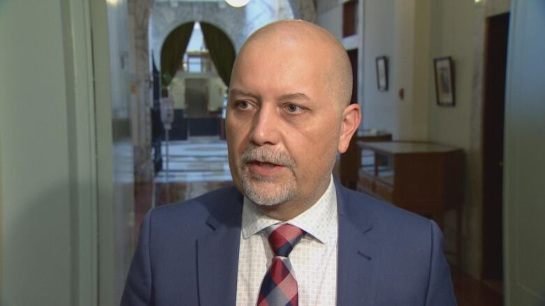 A man in a navy suit stands in the B.C. legislature.