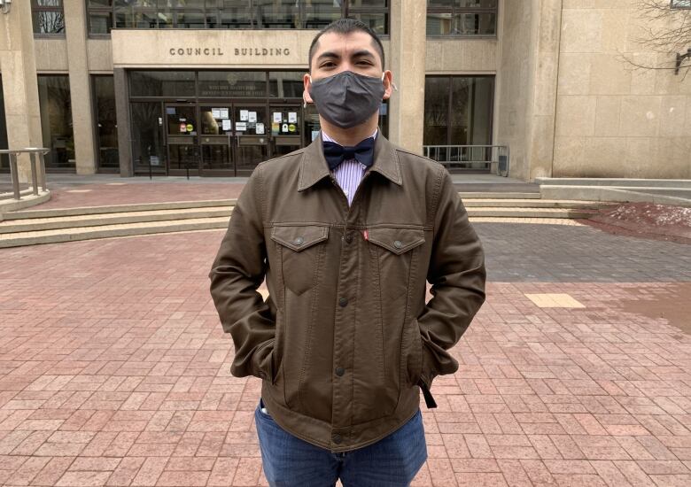 A man wearing a mask poses for a photo in front of Winnipeg city hall.