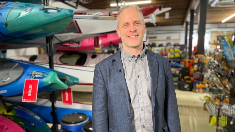 A man in a dark bluish blazer and grey button-up shirt stands in a wilderness supply store.