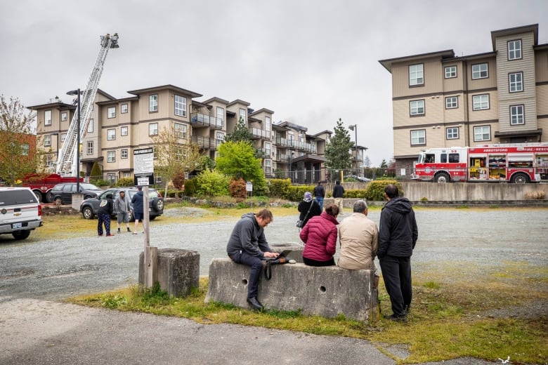 People stand at a barrier while a building behind them emits smoke.