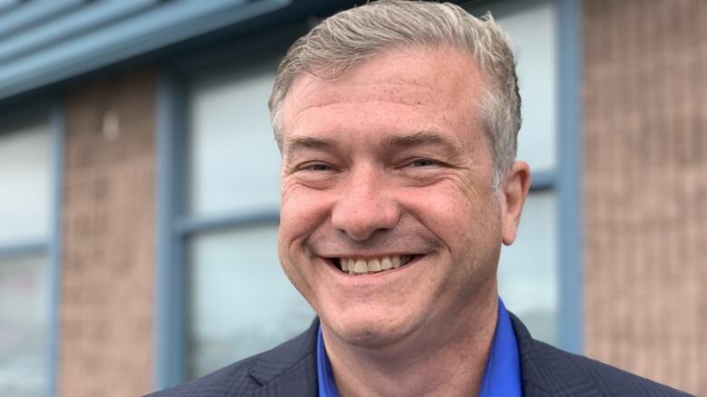 A man in a blue shirt smiles wide for a photo in spring.