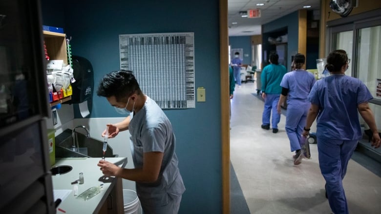 A hallway of nurses walk away as another nurse prepares medicine.