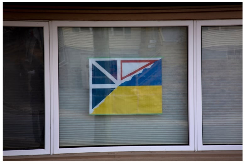 A half Newfoundland and Labrador, half Ukraine flag hangs in the window of a home.