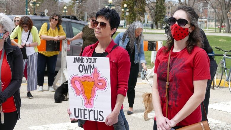 A person in a red shirt carries a sign that reads 