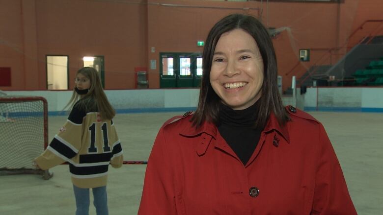 A woman smiles as she stands on the ice in a an arena