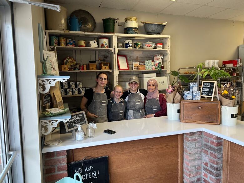 Four people in aprons stand behind a counter in a small shop.