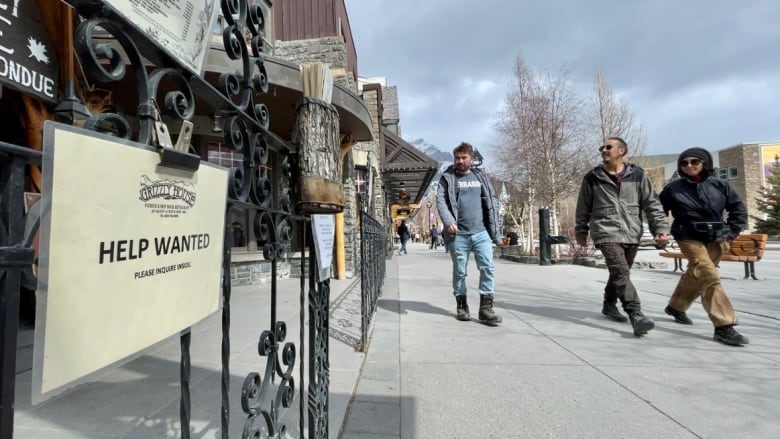 A help wanted sign is pictured Banff, Alta. as pedestrians look on.