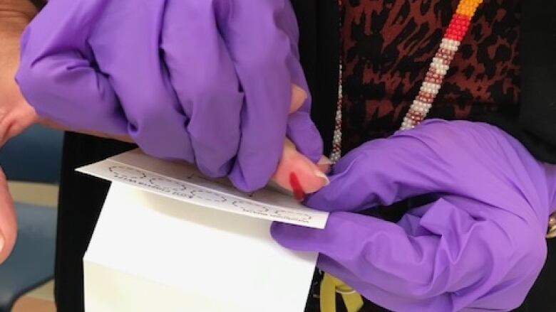 A health care provider wearing purple gloves performs a blood test by pricking someone's finger.