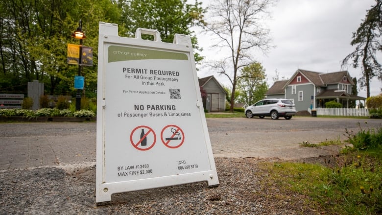 A city of Surrey billboard is posted on the sidewalk at Elgin Heritage Park. It says a permit is required for all group photography in this park.