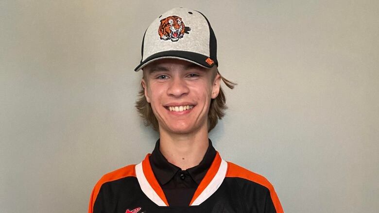 A smiling teenage boy wears a hockey jersey featuring a roaring tiger. 