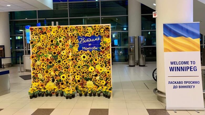 A board with sunflowers attached to it and a sign with a Ukrainian flag on it stand inside a building.