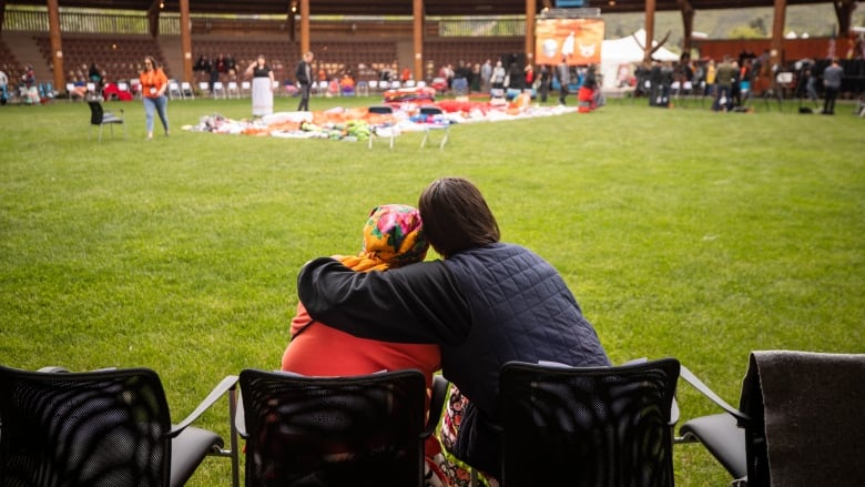 Two people sit in lawn chairs, one with their arm around the other