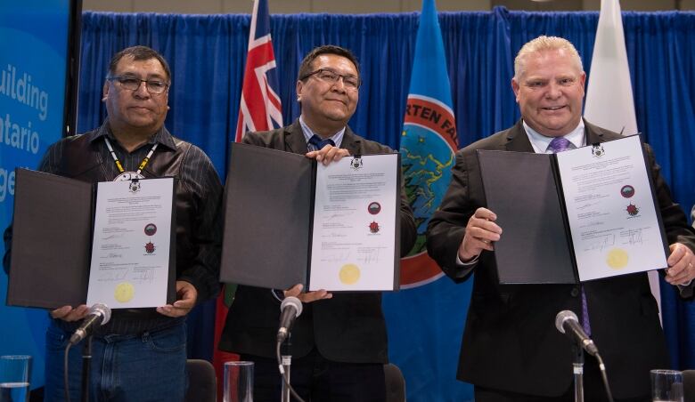 Three men wearing suits stand up and show a draft agreement in front of them.