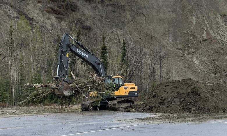 The photo shows an excavator cleaning trees and mud on a road. 