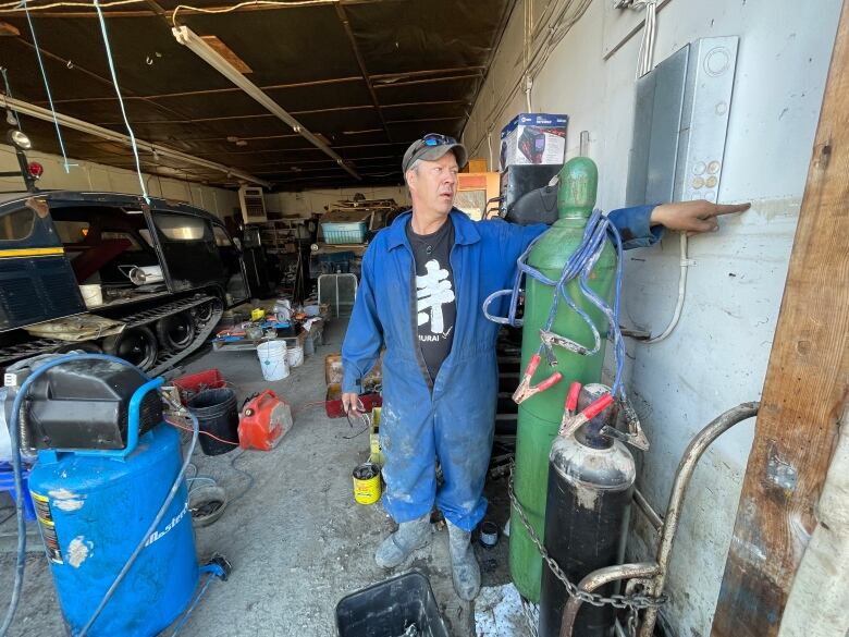 A man wearing a blue jump suit points at a wall 