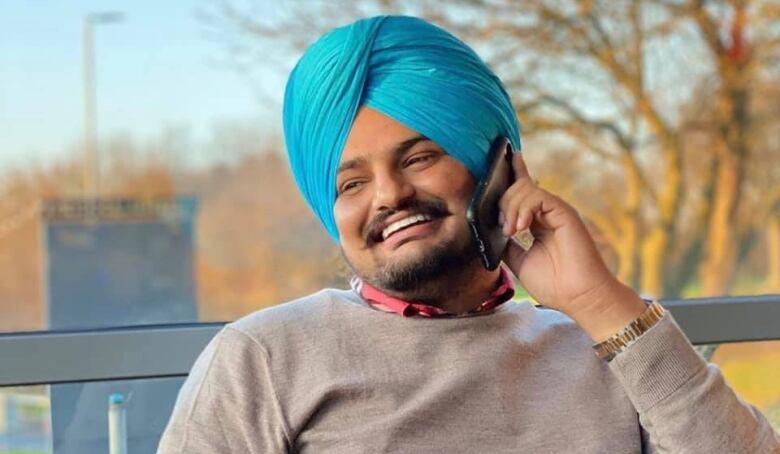 Rapper Sidhu Moose Wala smiles as he appears to speak into a cell phone. 