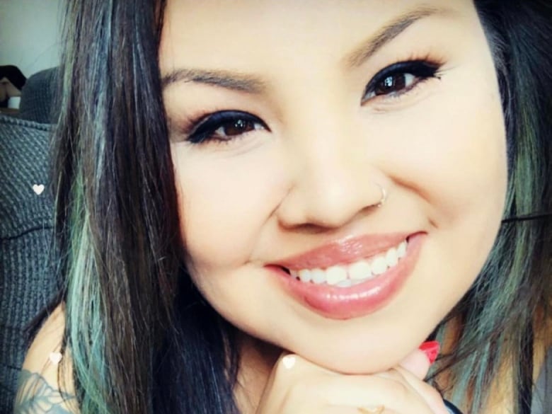 A woman smiles at the camera and leans forward, with her chin resting on her hand.