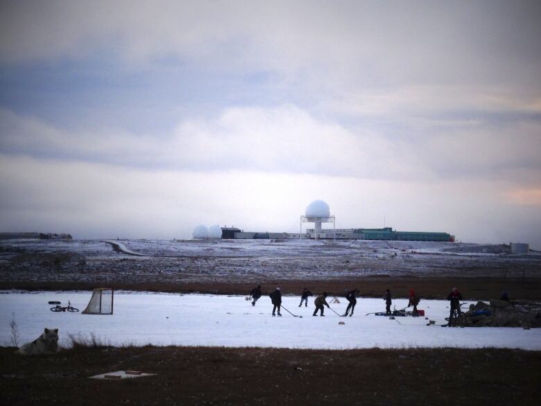 Kids play hockey on a pond in front of a satellite dish.