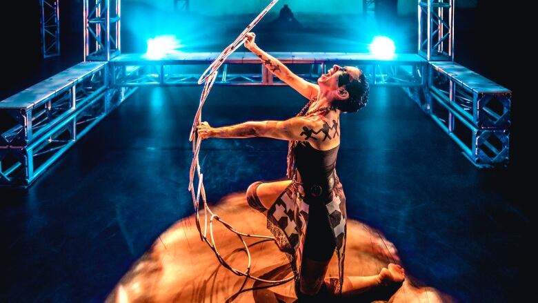 Indigenous dancer on her knees and holding up an object during a dance performance. 