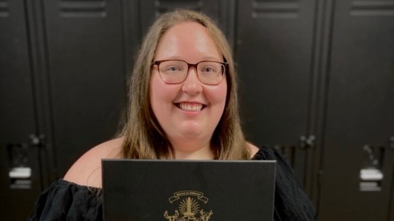 Kanessa Hanzlik, a young woman, holds up her diploma from Collge Boral.