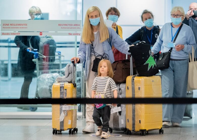 Several people carrying luggage walk through an airport.