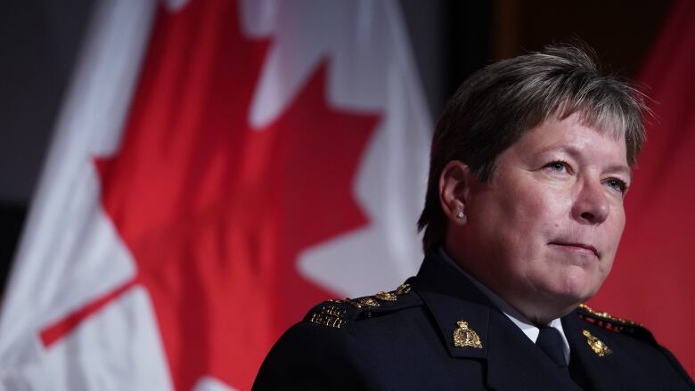 A woman in an RCMP uniform stands in front of a Canadian flag. 