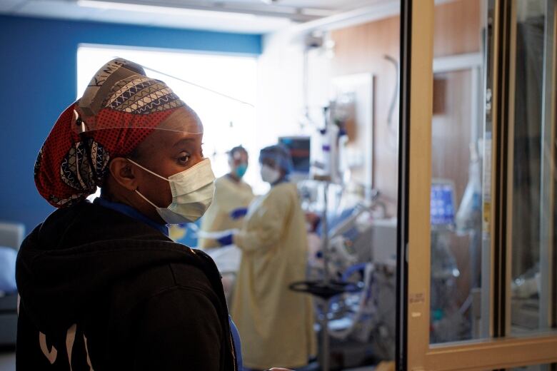 A nurse looks over her shoulder. She's standing in a hospital and wearing COVID-19 protective gear. 